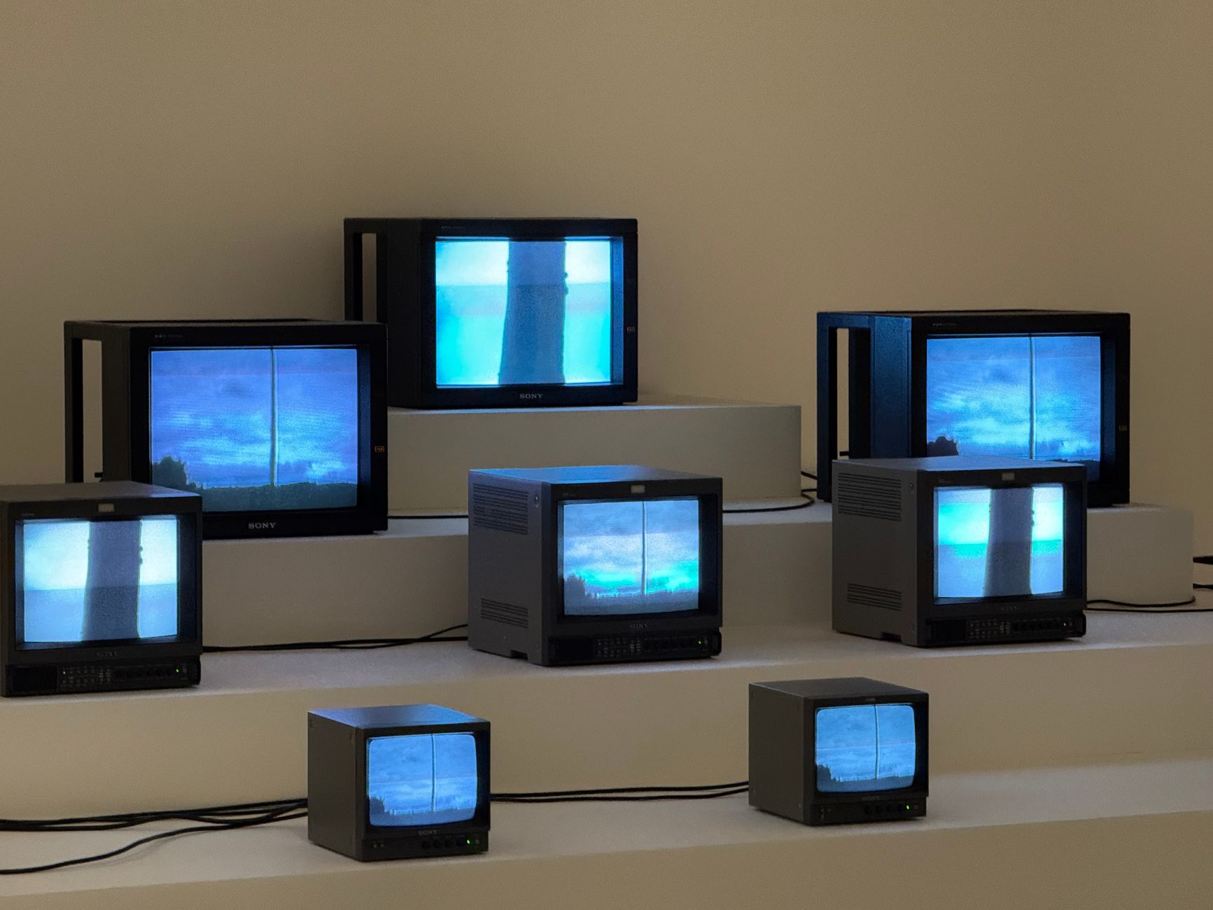 Artistic arrangement of vintage TVs displaying static and blue screens in a minimalist setting.
